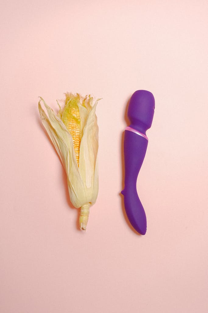 A creative still life concept featuring an ear of corn and a purple vibrator on a pastel background.