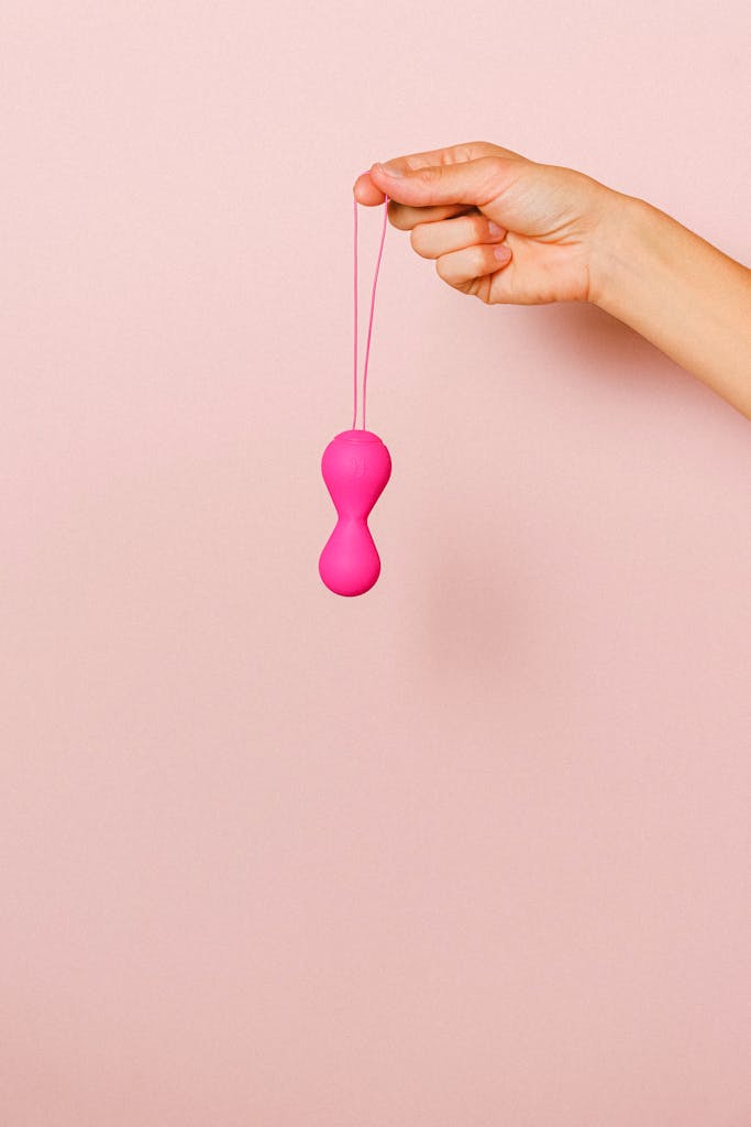 Close-up of a hand holding pink silicone ben wa balls against a pastel background.