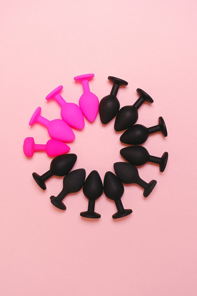 Colorful arrangement of silicone sex toys forming a circle on a pastel pink surface.